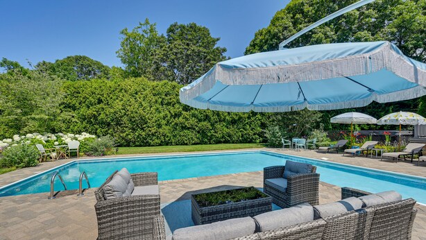 Piscina com mobiliário de vime e guarda-sóis, rodeada por vegetação.