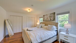 Quarto com cama grande, mesa de cabeceira, janela com persianas e porta.