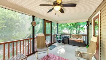 A covered porch with a ceiling fan, wicker chairs, a small table, and a view of the surrounding greenery.