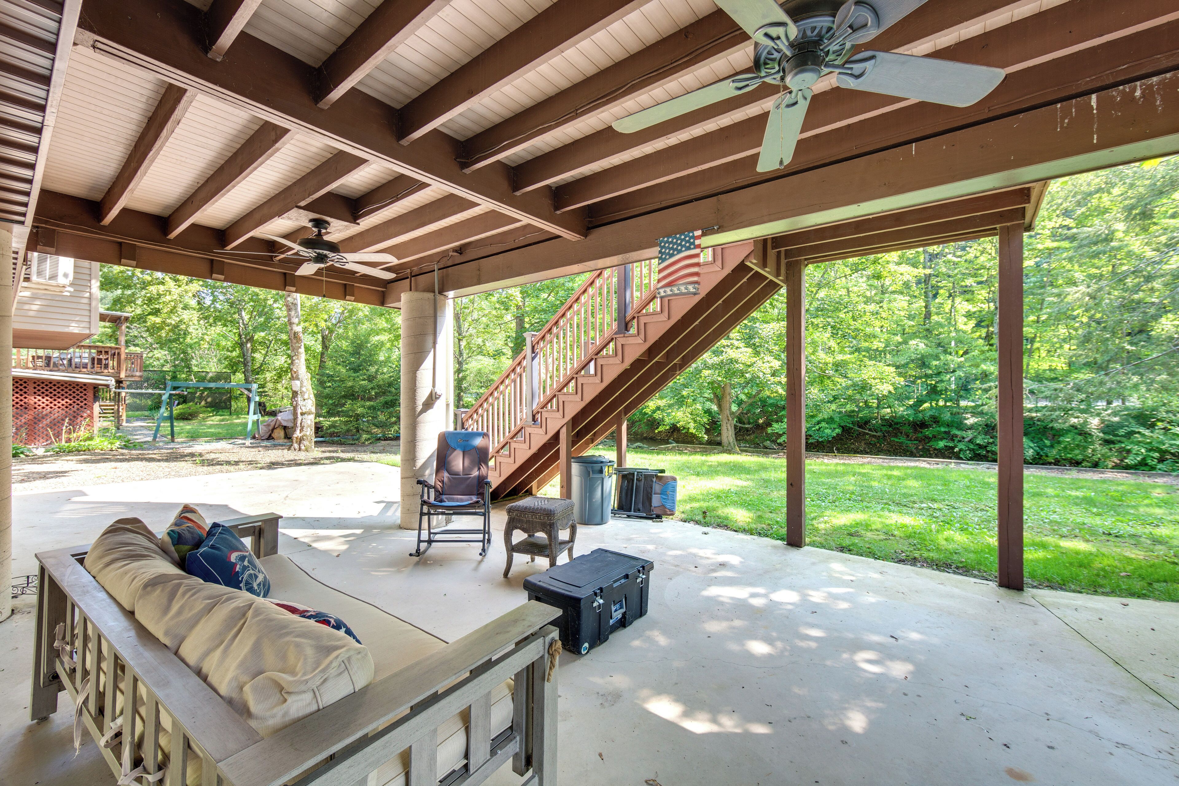 A covered outdoor patio with a wooden bench, a table, a suitcase, and a chair.