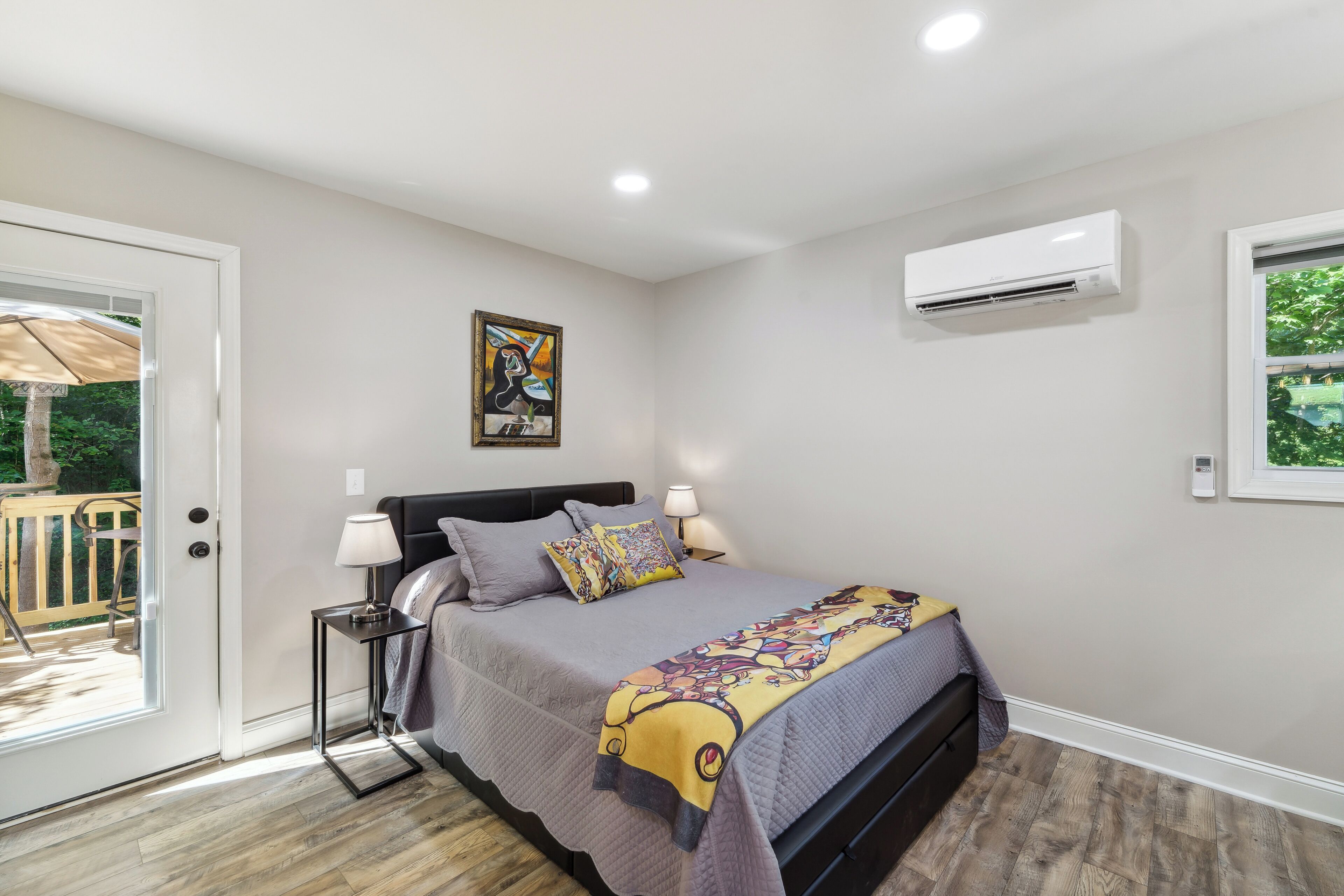 A bedroom with a bed, bedside tables, an air conditioner, a window, and a door leading to an outdoor area.