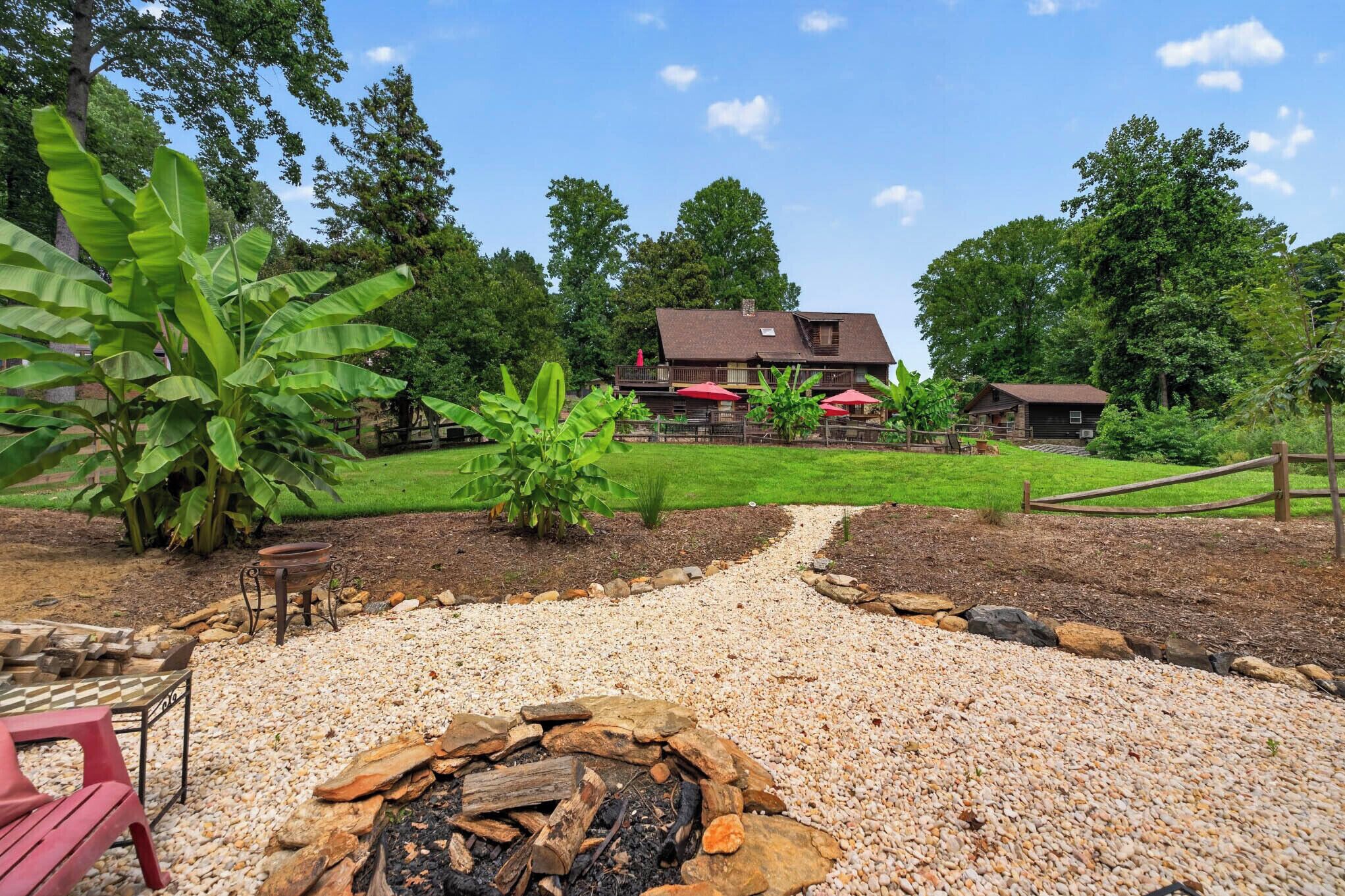 A backyard with a fire pit, a dining area, and a house with a red umbrella.