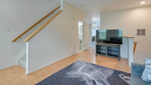 A spacious living area with a wooden staircase, a flat-screen TV on a stand, and a grey rug. - Owings Mills Townhouse: 8 Mi to Liberty Reservoir! (Owings Mills)