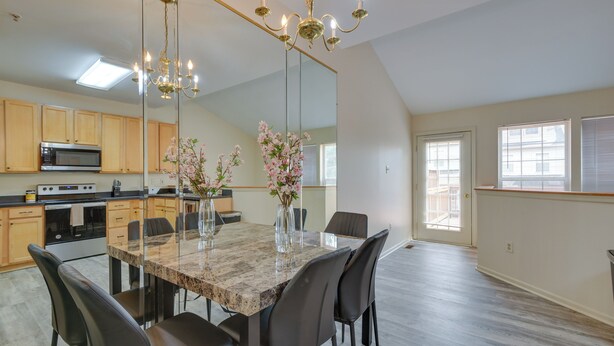 A modern kitchen with a dining area, featuring a large mirror, a chandelier, and a central island with chairs. - Owings Mills Townhouse: 8 Mi to Liberty Reservoir! (Owings Mills)