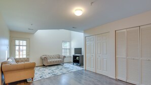 A spacious living room with hardwood flooring, a beige sofa, a television, and a large closet. - Owings Mills Townhouse: 8 Mi to Liberty Reservoir! (Owings Mills)