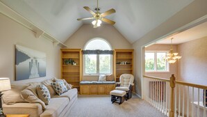 A cozy room with a high ceiling, a ceiling fan, a large window, a cushioned bench, a chair, and a staircase with a railing. - Sibley Home w/ Game Room & Expansive Yard! (Sibley)