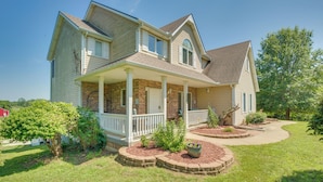 A two-story house with a front porch, brick foundation, and a landscaped yard with a tree and flower bed. - Sibley Home w/ Game Room & Expansive Yard! (Sibley)