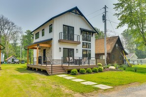 A two-story house with a balcony, a covered porch, and a stone foundation. - Modern Lake Ontario Escape w/ Beach Access! (Henderson)
