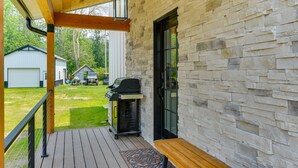 Una terraza techada con pared de piedra, una parrilla y un banco.