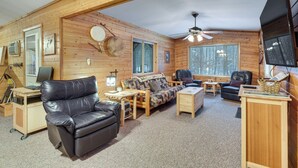 Ein Holzblockhaus-Interieur mit Ledersofa, Couchtisch aus Holz, Kamin und Fernseher.