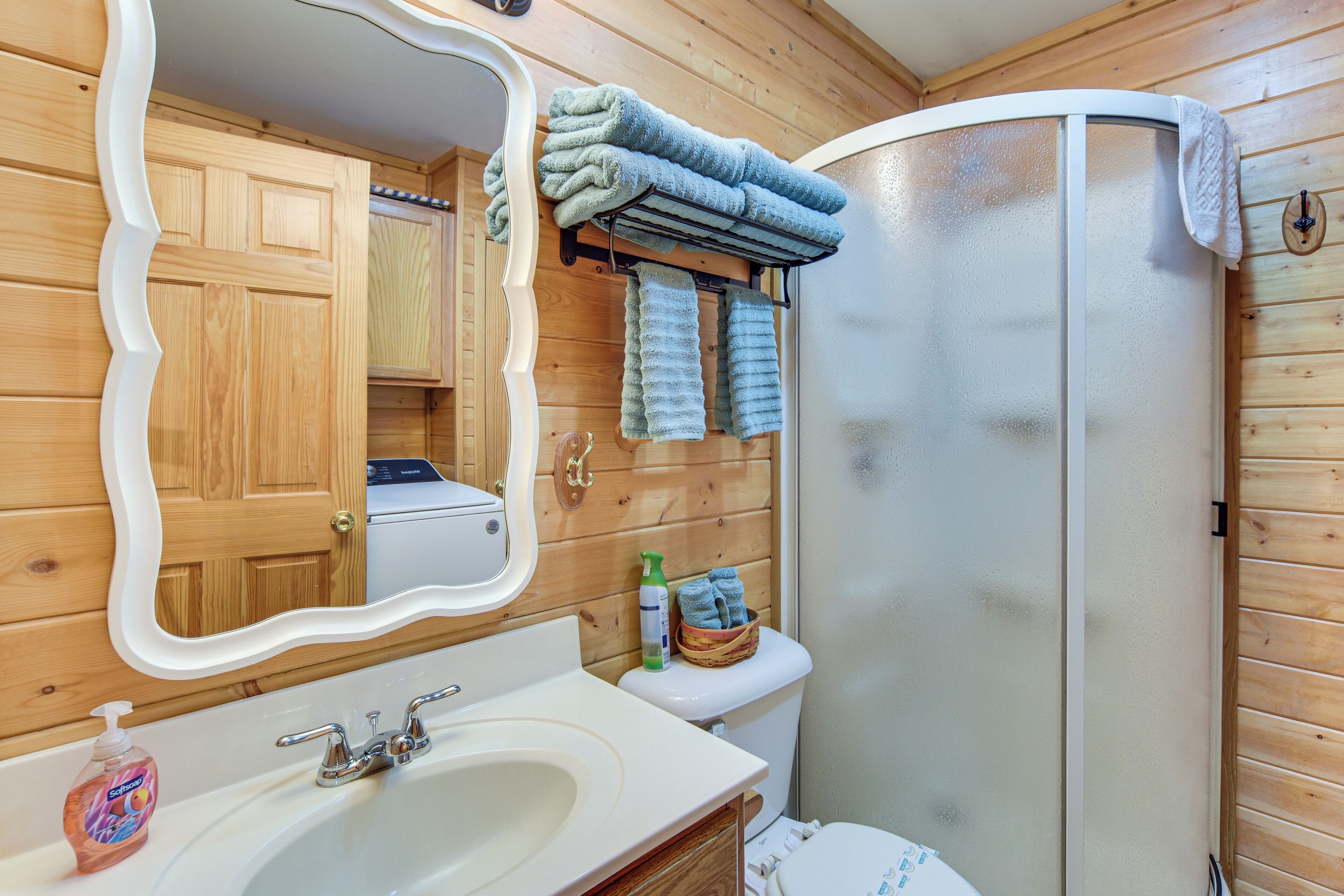 A bathroom with wooden walls, a white sink, a mirror, a toilet, and a shower.