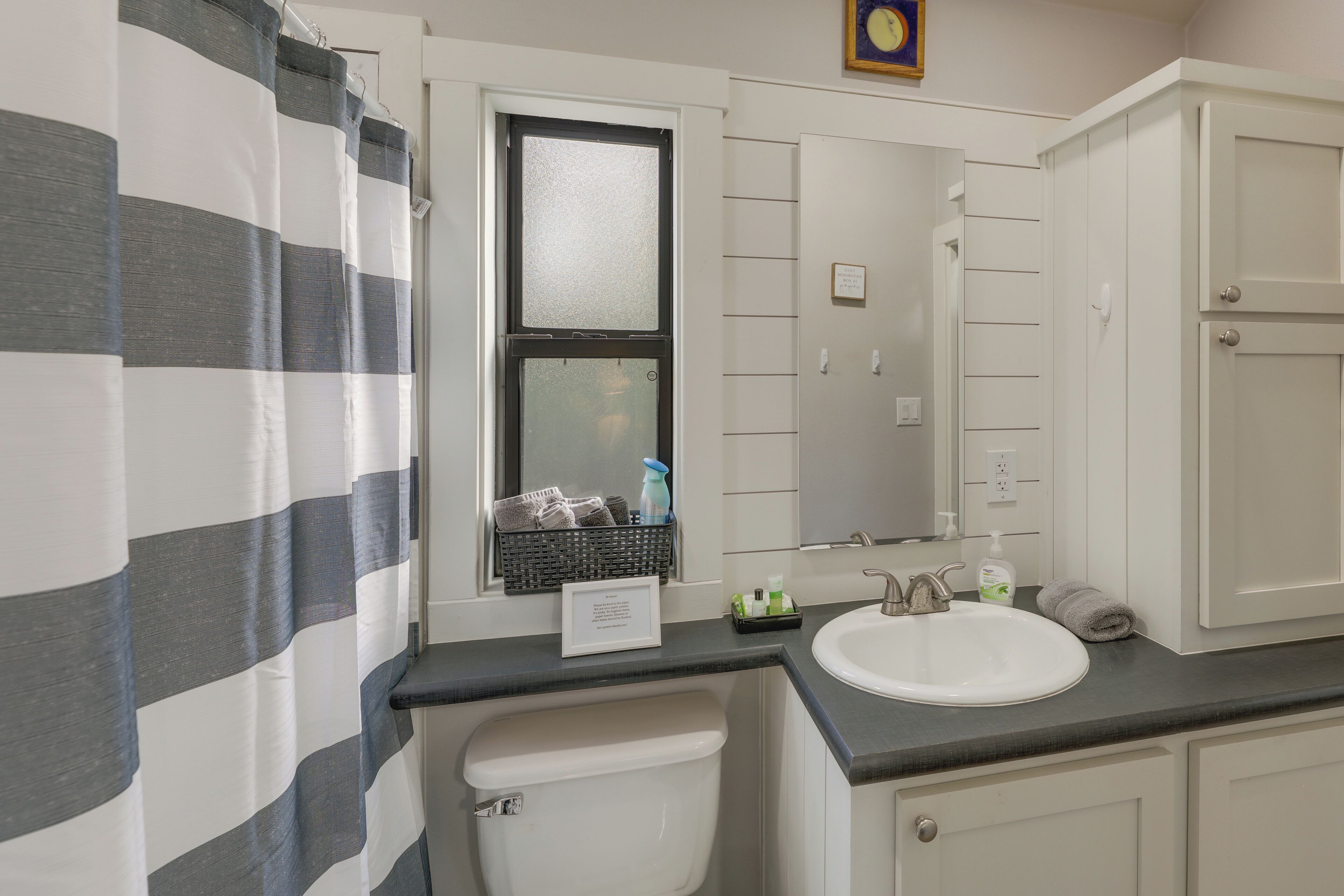 A bathroom with a striped shower curtain, a window with a view, a sink, and a mirror.