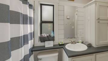 A bathroom with a striped shower curtain, a window with a view, a sink, and a mirror.