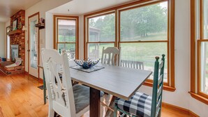 Un comedor con una mesa de madera, sillas blancas y vista a un patio cubierto de césped a través de amplios ventanales.