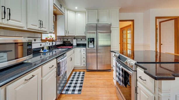 Una cocina moderna con armarios blancos, electrodomésticos de acero inoxidable y un tapete de piso a cuadros.