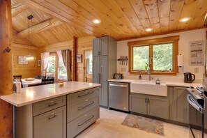 A kitchen with wooden ceiling beams, a window with curtains, a sink, and a toaster. - Alexandria Cabin w/ Patio, Grill & Deck (Bristol)