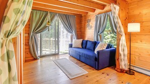 A cozy cabin interior with a blue sofa, wooden floors, and a large window with curtains. - Alexandria Cabin w/ Patio, Grill & Deck (Bristol)