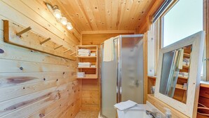 A wooden cabin bathroom with a built-in shower, a glass-enclosed toilet, and a sink with a soap dispenser. - Cozy Cora Studio Cabin w/ Wind River Mtn Views (Cora)