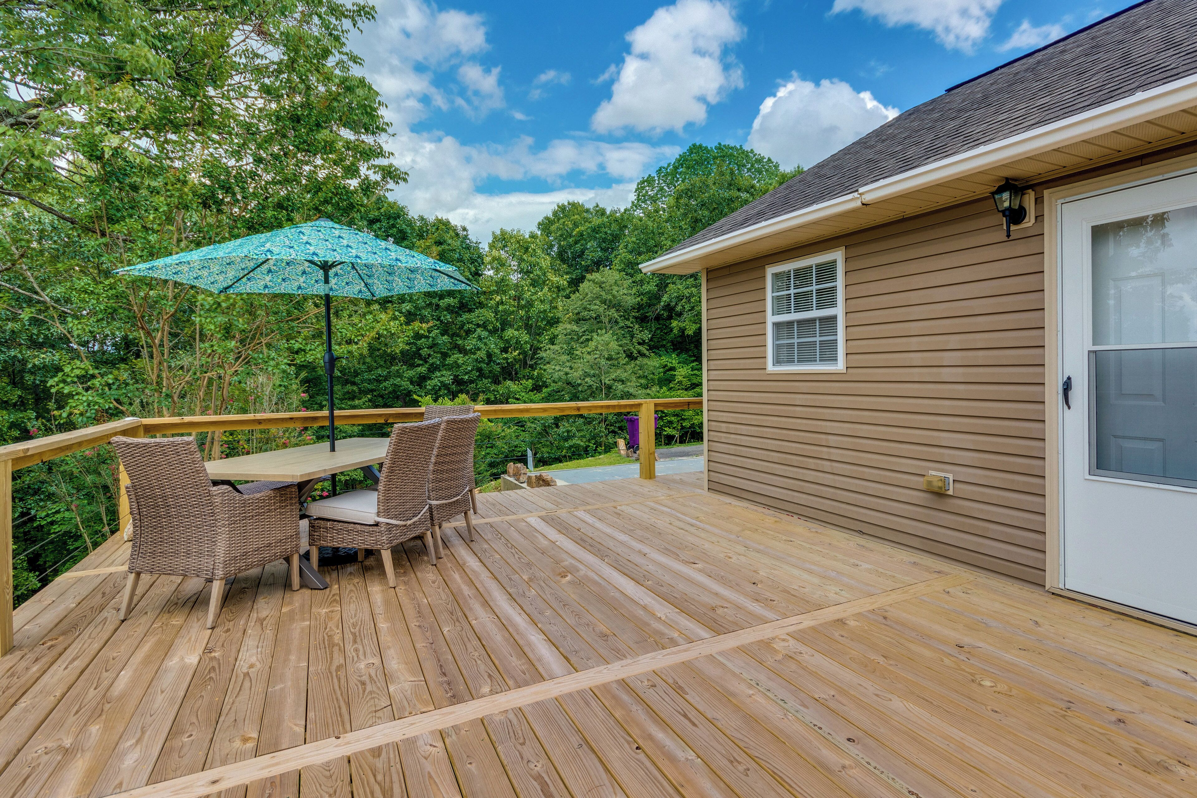 A wooden deck with a table and chairs, a blue umbrella, and a house in the background.