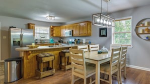 A kitchen with wooden cabinets, a stainless steel refrigerator, a dining table with chairs, and a window with blinds. - Searcy Vacation Rental w/ Deck & Water Views! (Searcy)