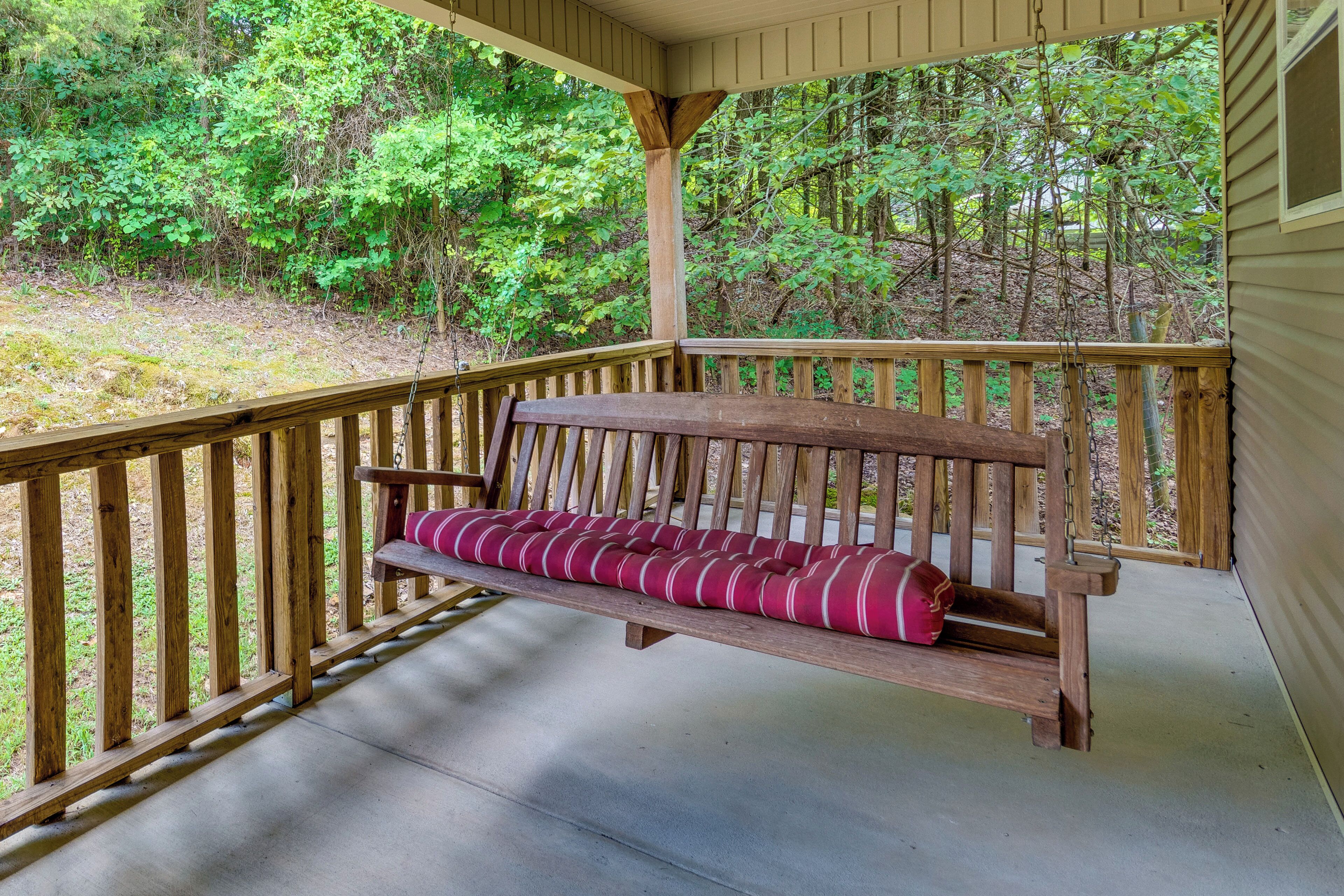 A wooden porch with a bench and a view of a forested area.