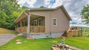 A two-story house with a covered porch, a small outdoor seating area, and a statue in the front yard. - Searcy Vacation Rental w/ Deck & Water Views! (Searcy)