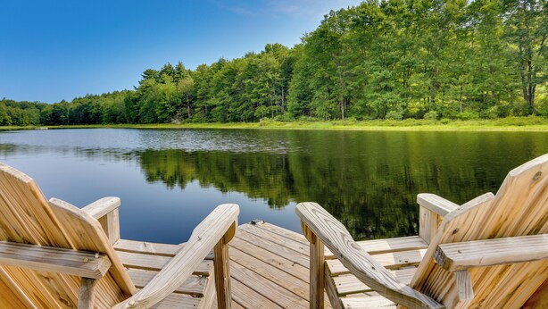 A wooden dock with chairs facing a calm lake surrounded by dense green trees. - Lakefront Catskills Container Home: Private Lake (Swan Lake)