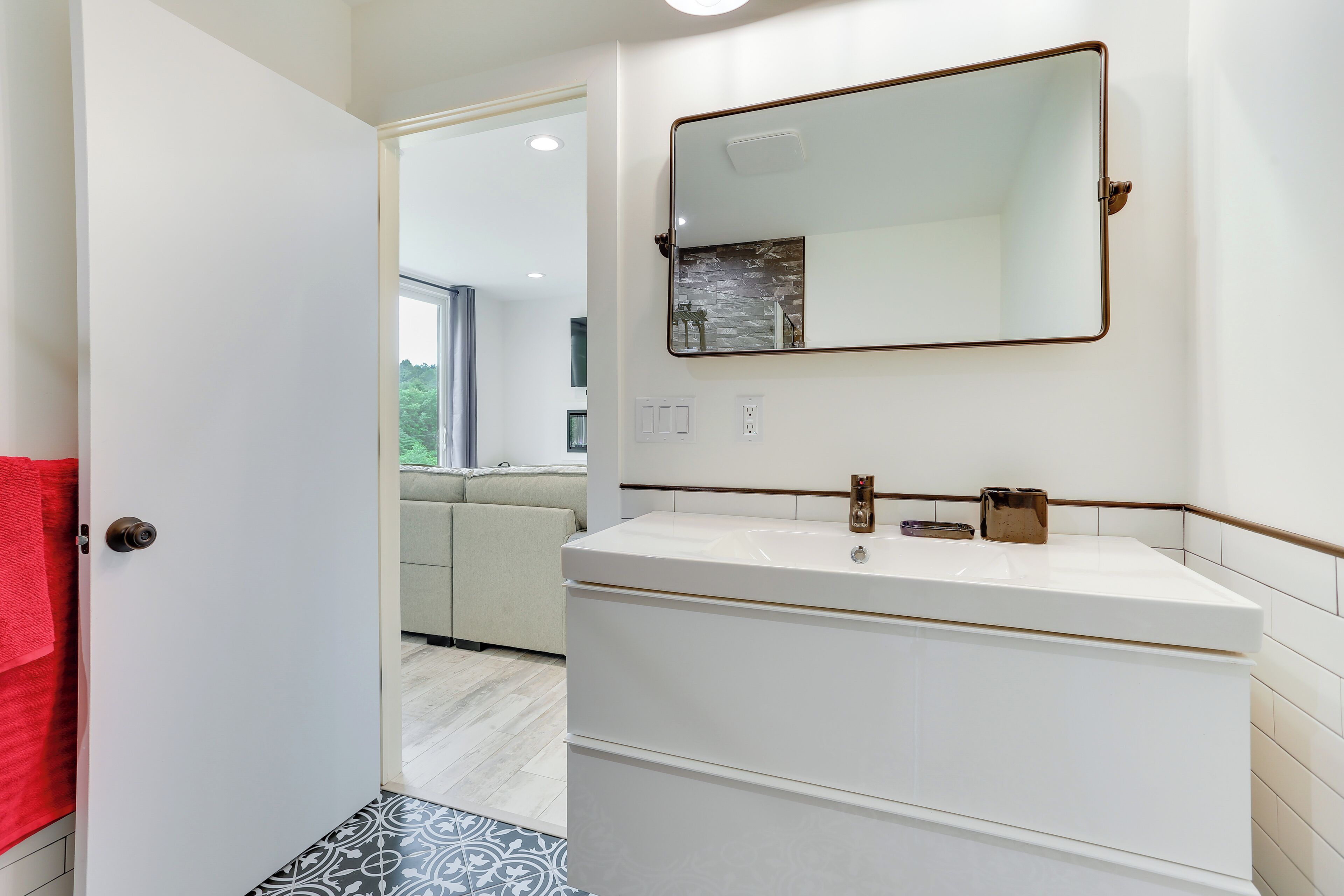 A bathroom with a white sink, a large mirror, and a red towel on the door.