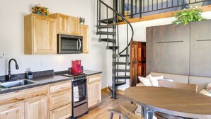 A modern kitchen with wooden cabinets, a built-in microwave, a red coffee maker, and a spiral staircase leading to a loft area. - Pet-friendly Elmo Home w/ Mountain & Lake Views! (Elmo)
