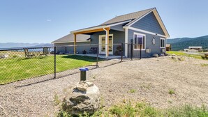 A single-story house with a covered porch, a fenced yard, and a view of mountains in the background. - Pet-friendly Elmo Home w/ Mountain & Lake Views! (Elmo)