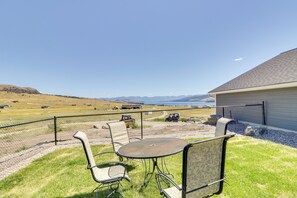 A fenced outdoor patio with a table and chairs, overlooking a rural landscape with mountains and a body of water. - Pet-friendly Elmo Home w/ Mountain & Lake Views! (Elmo)