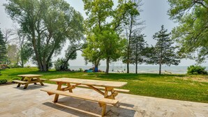 A picnic area with wooden tables and benches, surrounded by trees and a view of the water. - Cozy Beachfront Cottage on Lake Ontario! (Henderson)