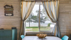 A dining area with a wooden table, teal chairs, and a view of the lake. - Cozy Beachfront Cottage on Lake Ontario! (Henderson)