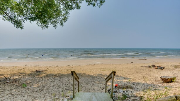 A beach with a wooden staircase leading to the water, surrounded by rocks and sparse vegetation. - Cozy Beachfront Cottage on Lake Ontario! (Henderson)