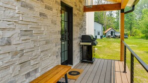 A covered porch with stone walls, a grill, and a view of a house in the background. - Spacious Lake Ontario Getaway: Steps to Beach! (Henderson)