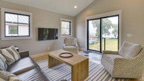 A modern living room with a sofa, armchair, and coffee table, large windows, and a flat-screen TV. - Spacious Lake Ontario Getaway: Steps to Beach! (Henderson)