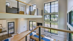 A spacious, multi-level interior with a kitchen, dining area, and a balcony with large windows. - Spacious Lake Ontario Getaway: Steps to Beach! (Henderson)