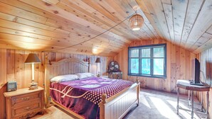 Une chambre à coucher aux murs lambrissés, avec un lit, des lampes de chevet, une commode, une table et une fenêtre.