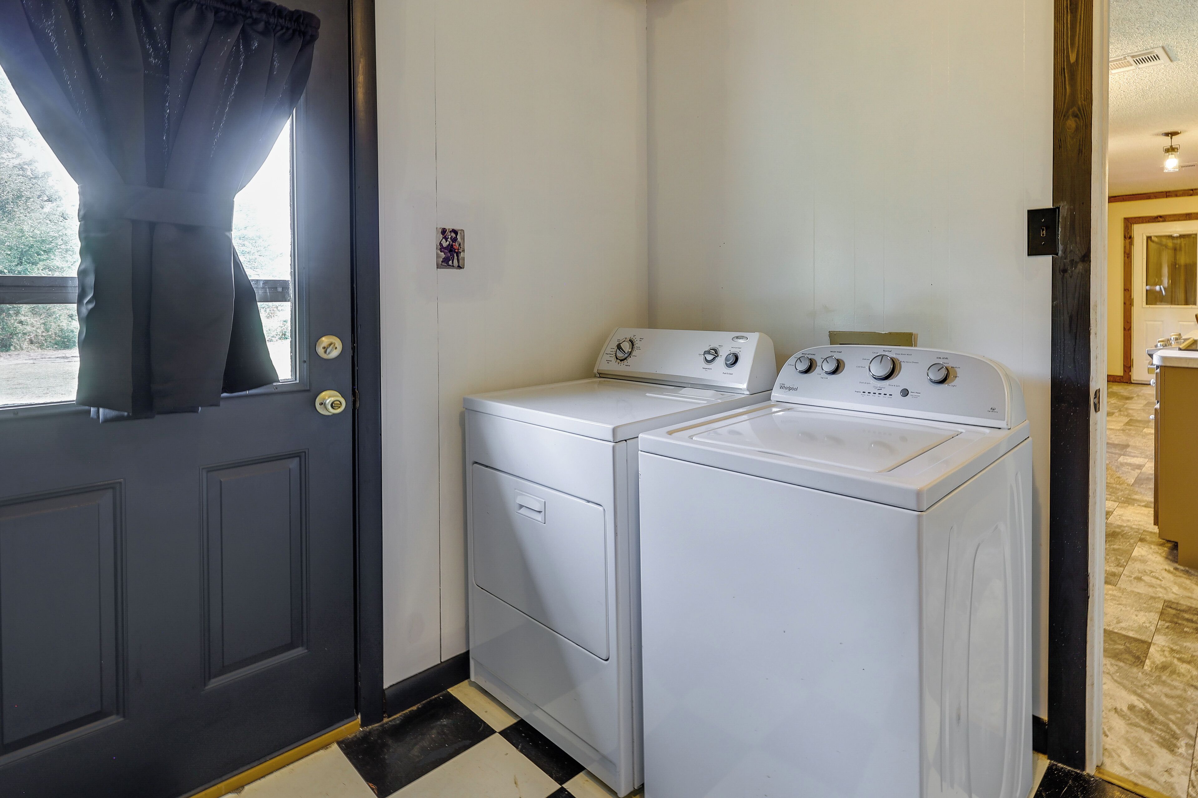 Une buanderie avec deux machines à laver blanches, un sol à carreaux noirs et blancs et une porte avec un rideau noir.