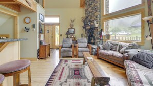 A cozy living room with a stone fireplace, wooden furniture, and a large window overlooking a scenic view.