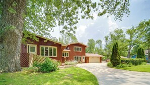 A two-story house with a garage, surrounded by a well-maintained lawn and mature trees. - Group-friendly Lake Erie Getaway w/ Private Yard (Conneaut)