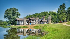 A Tudor-style building with a tower, situated next to a pond with a clear reflection.