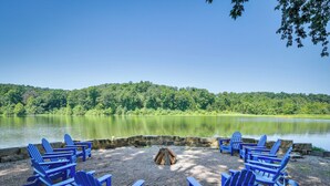 A lakeside seating area with Adirondack chairs arranged around a fire pit.