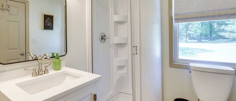 A bathroom with a white sink, mirror, shower, and toilet.