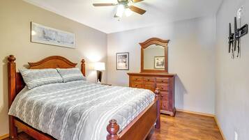 A bedroom with a wooden bed, a ceiling fan, a dresser, and a wall-mounted mirror.