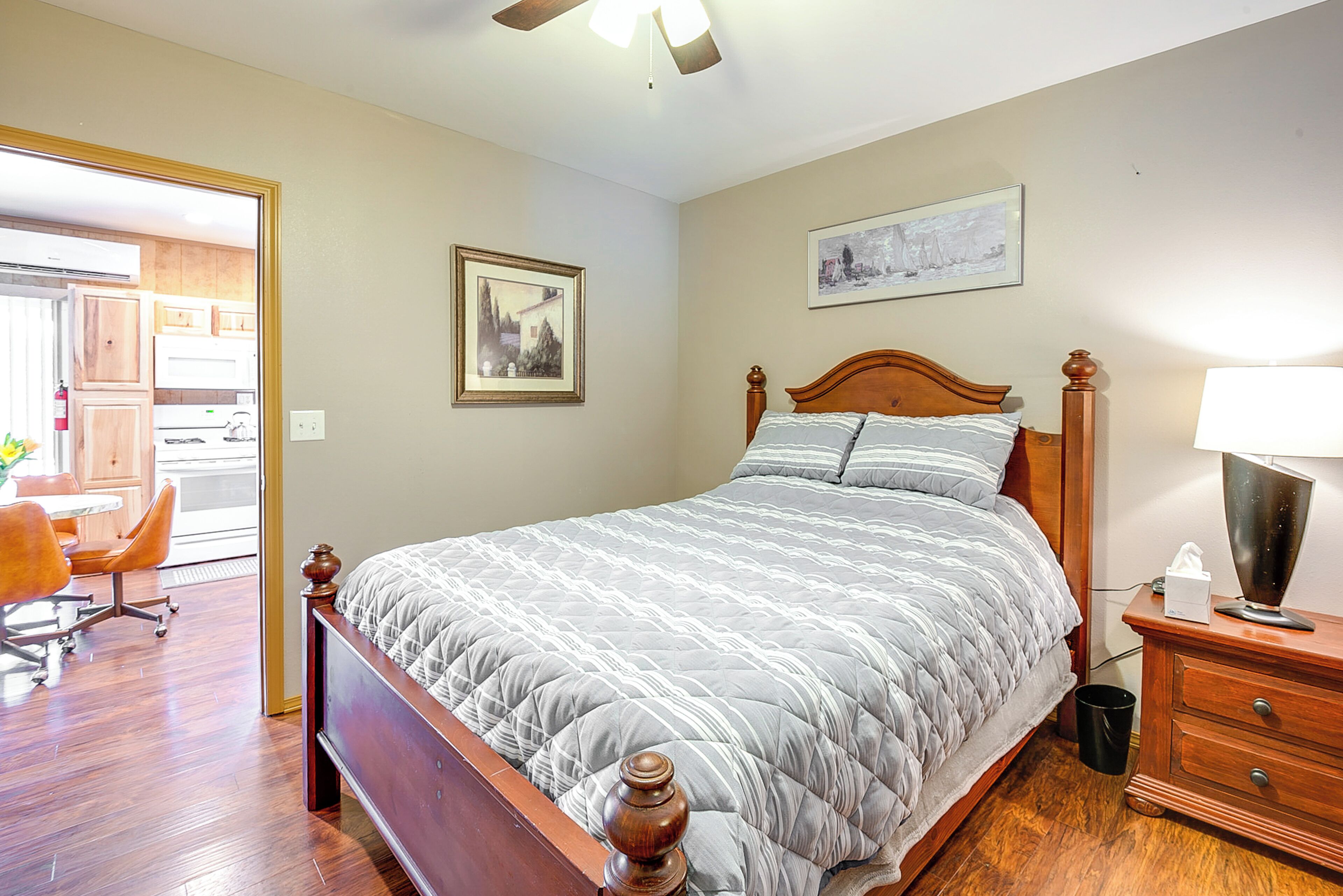 Quarto com cama de madeira, mesa de cabeceira, cadeira e porta para um banheiro.
