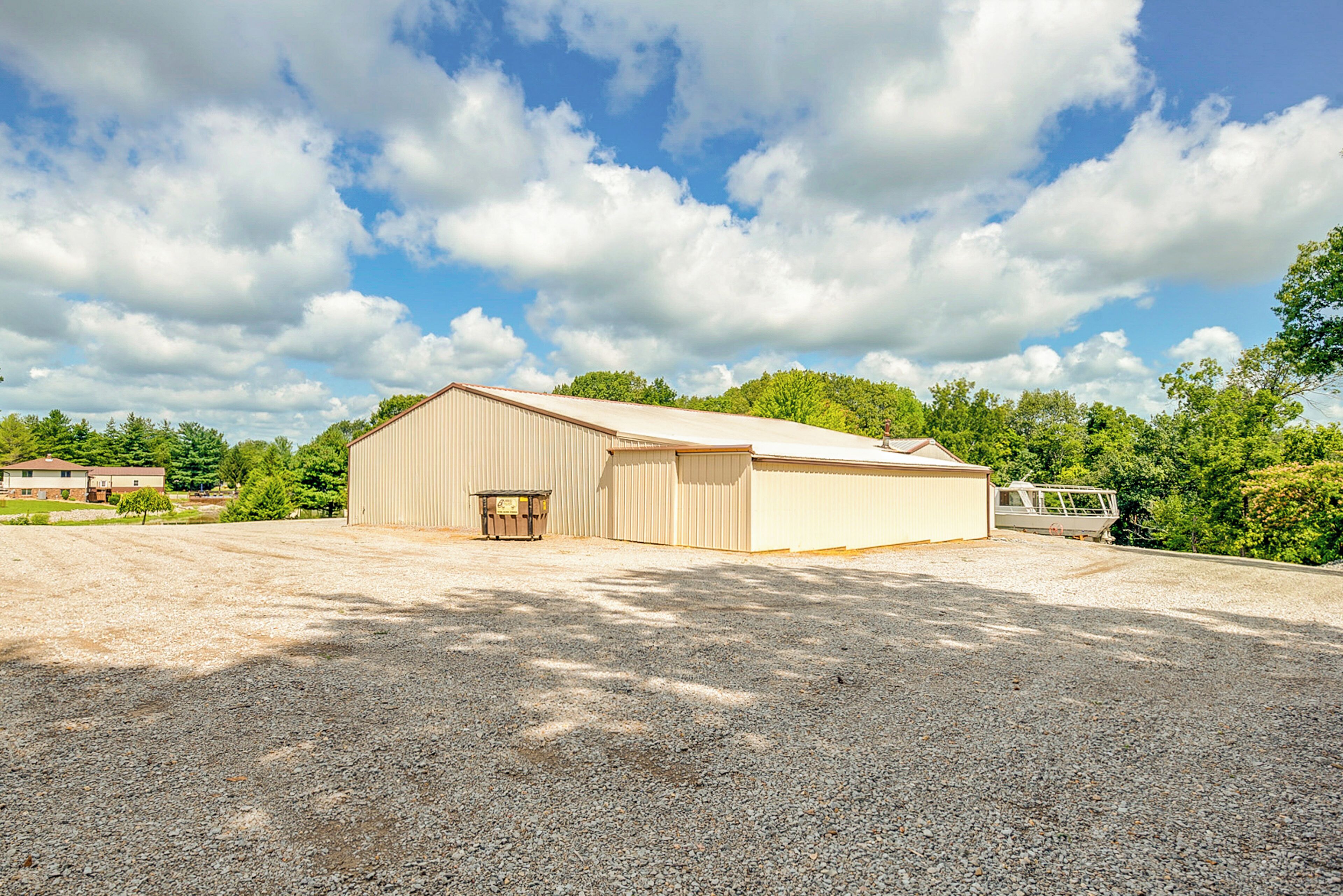 A large, single-story building with a flat roof, likely a warehouse or storage facility, surrounded by a gravel driveway and trees.
