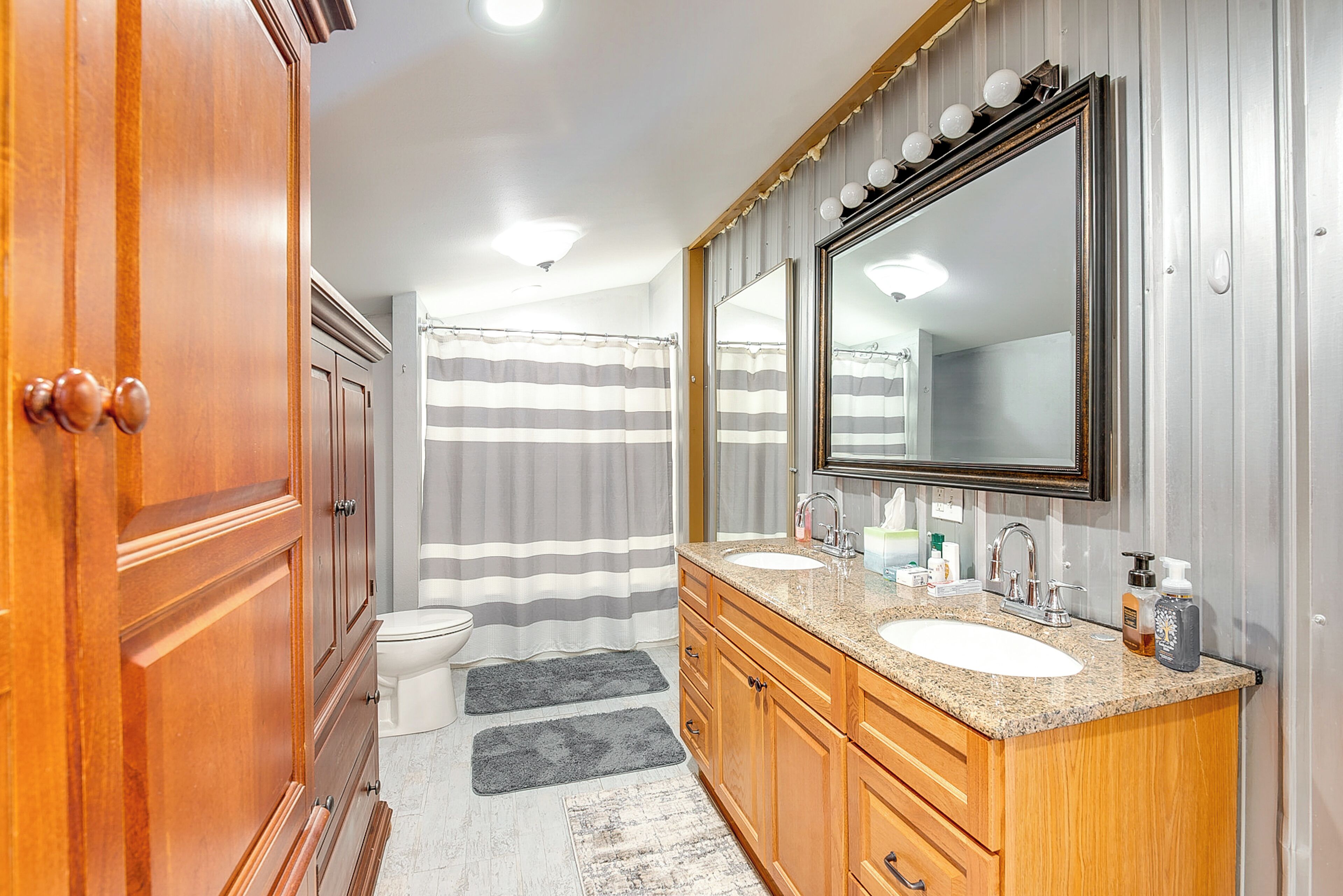 Une salle de bain avec des meubles en bois, un lavabo double, un grand miroir et un rideau de douche à rayures.