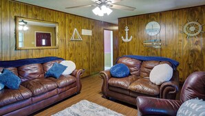 A room with two leather sofas, a ceiling fan, wooden walls, and nautical-themed decorations. - Pet-friendly Cartwright Home w/ Private Backyard! (Cartwright)
