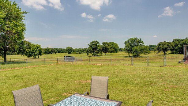 An outdoor seating area with a table and chairs, surrounded by a grassy field and trees. - Pet-friendly Cartwright Home w/ Private Backyard! (Cartwright)